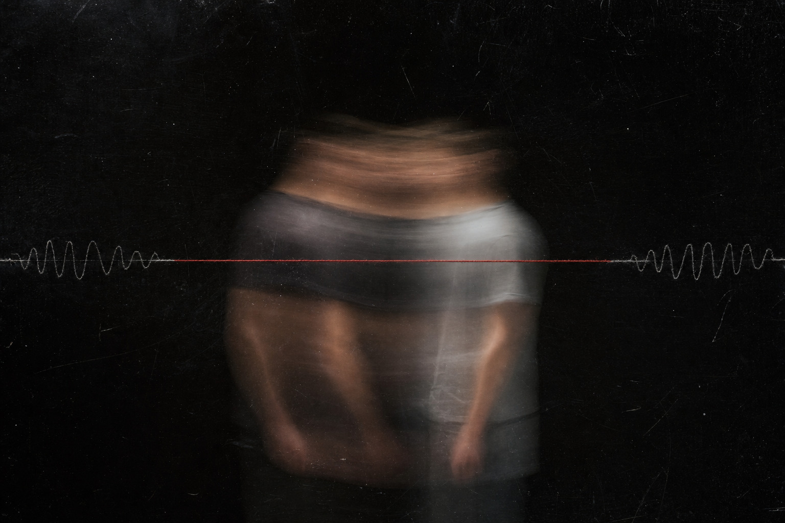 Two blurred human figures overlap behind dark glass while one red line crosses their shared outline.