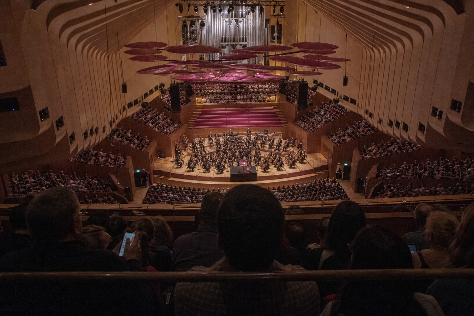 An imperfect audience photograph looks down from the dress circle towards the orchestra and central production desk.
